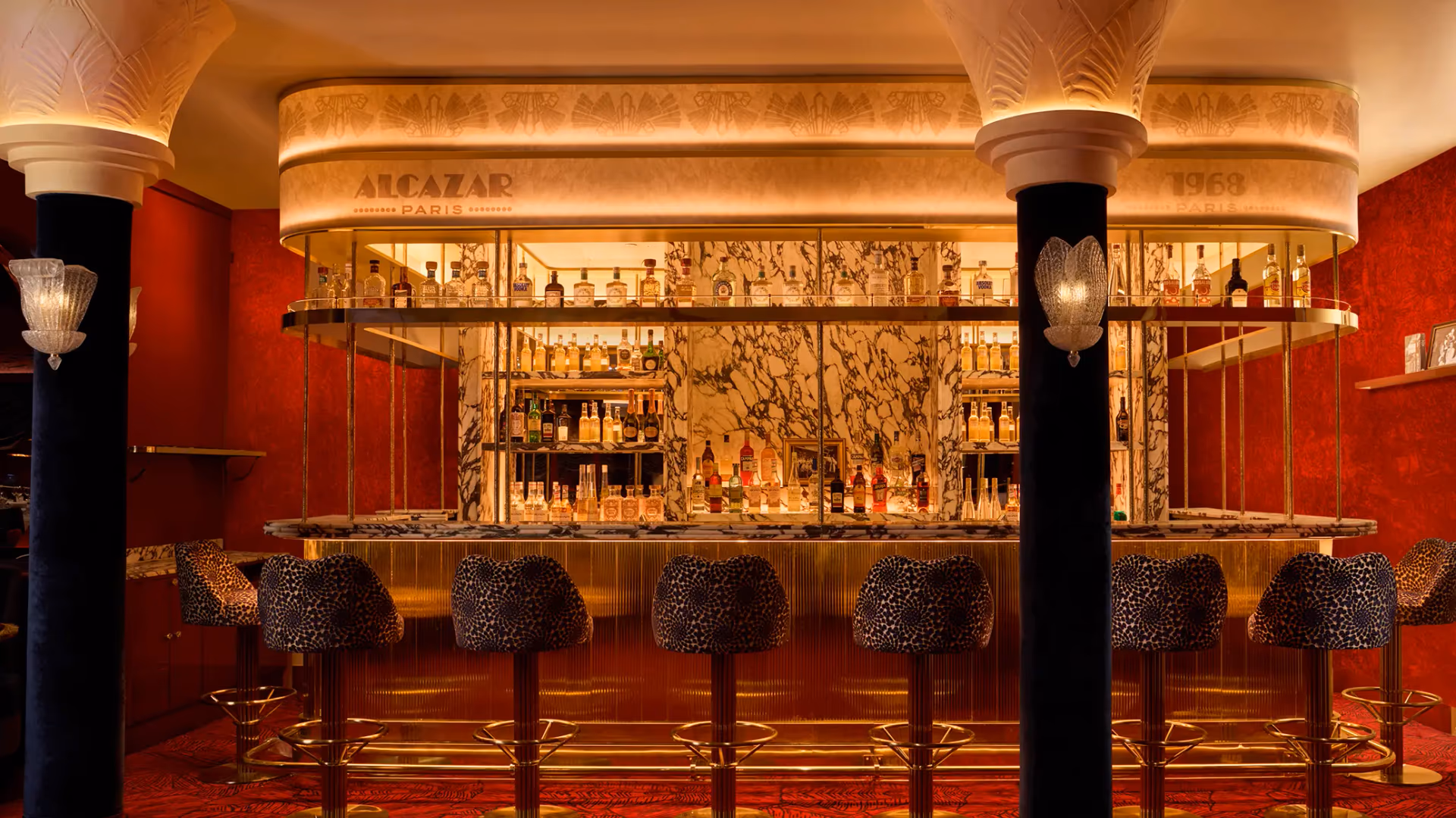 Bar avec étagères remplies de bouteilles d'alcool, tabourets à motifs et décoration murale rouge et or