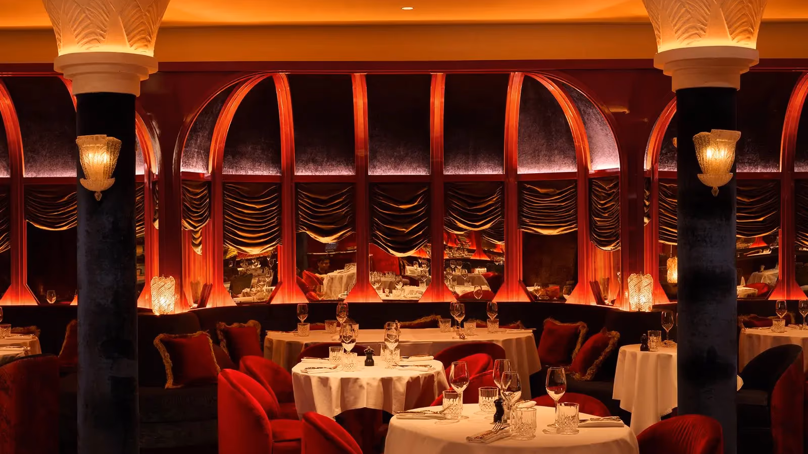 Restaurant élégant avec des tables dressées, des sièges rouges et des arches décoratives éclairées en rouge et or