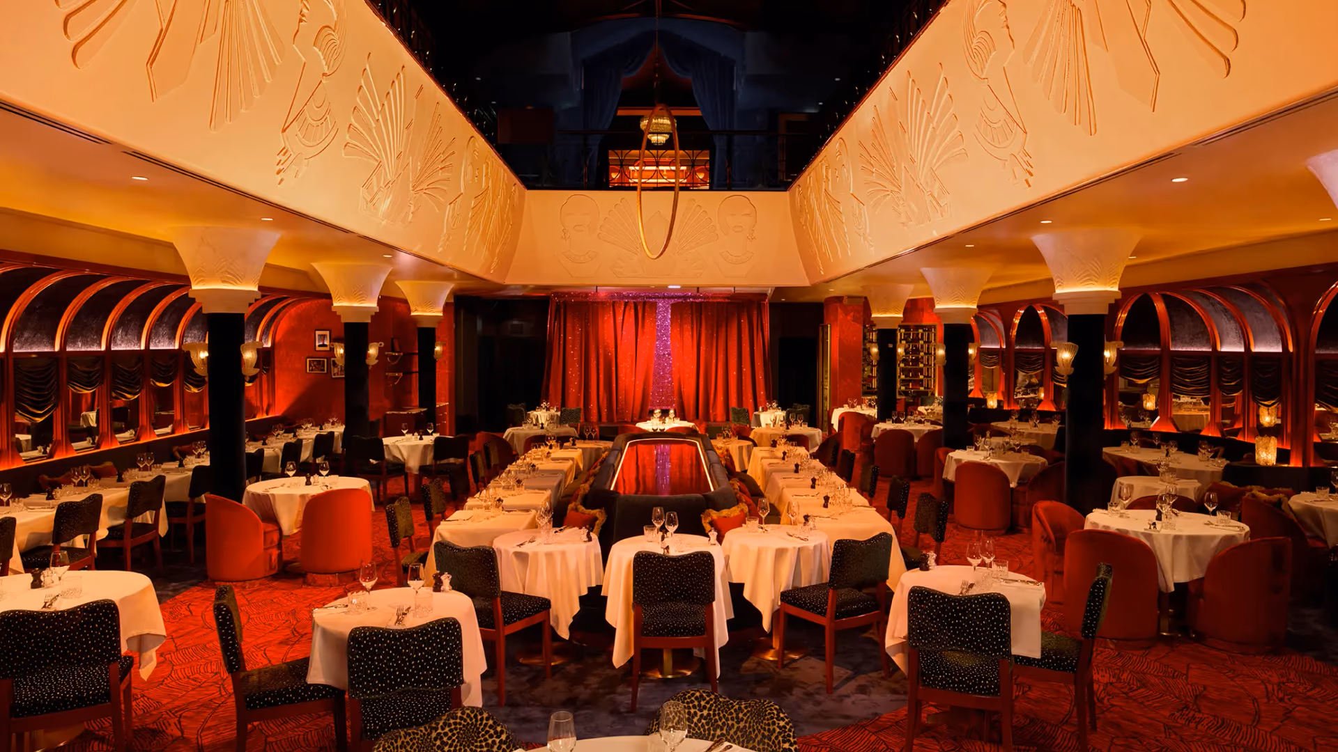 Elegant restaurant room with set tables, red and green chairs, black columns, and walls decorated with red and black curtains.